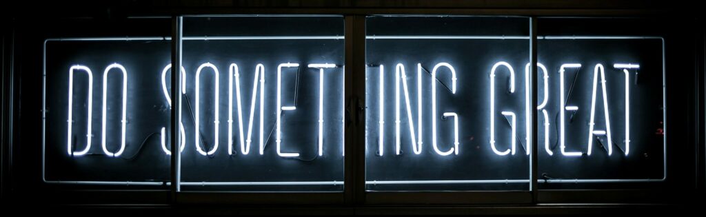 A neon sign on a black background that says, "Do Something Great", the slogan for IIBEC's Project Excel.