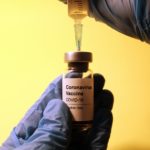 gloved hand holding bottle labeled coronavirus vaccine with syringe